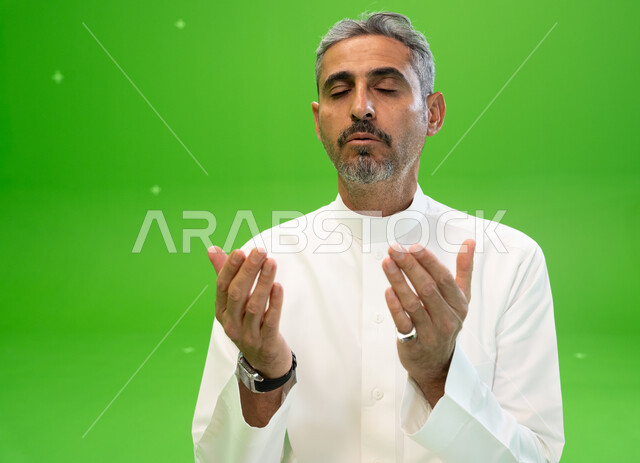 التذلل و الطلب من الله تعالى, التقرب الى الله بالأعمال الصالحة، كروما مقربة لرجل عربي خليجي سعودي يرتدي الزي التقليدي يرفع يديه ويدعي بإيماءات التوسل و الخشوع، اسلاميات وعبادة، خلفية خضراء