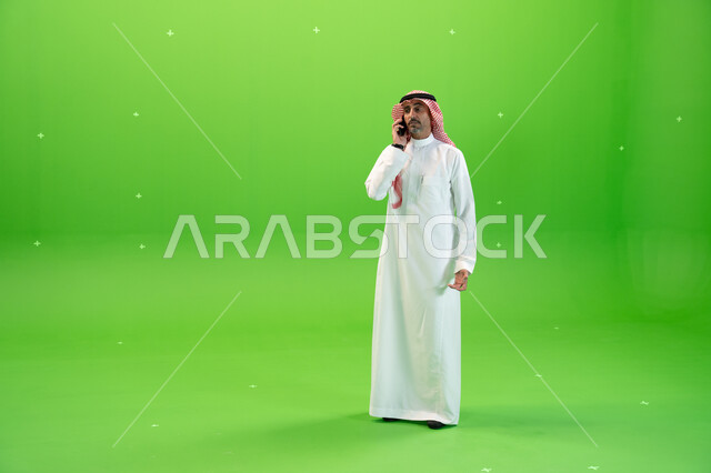 مفهوم صلة الرحم، الاتفاق على موعد عمل، كروما لرجل عربي خليجي سعودي يرتدي الثوب والشماغ السعودي يقوم بإجراء مكالمة صوتيه عبر الهاتف المحمول، التواصل مع الأصدقاء والأقارب بإيماءات السعادة، صورة الجسم بالطول الكامل، خلفية خضراء