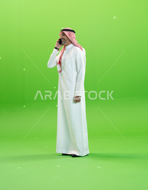 مفهوم صلة الرحم، الاتفاق على موعد عمل، كروما لرجل عربي خليجي سعودي يرتدي الثوب والشماغ السعودي يقوم بإجراء مكالمة صوتيه عبر الهاتف المحمول، التواصل مع الأصدقاء والأقارب بإيماءات السعادة، صورة الجسم بالطول الكامل، خلفية خضراء