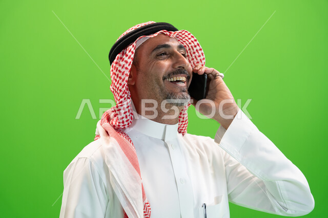 Exchanging amusing and funny conversations, laughing and communicating with friends and relatives with gestures of happiness, the concept of kinship, a close-up of a Saudi Arabian Gulf man wearing the Saudi thobe and shemagh making a voice call via mobile