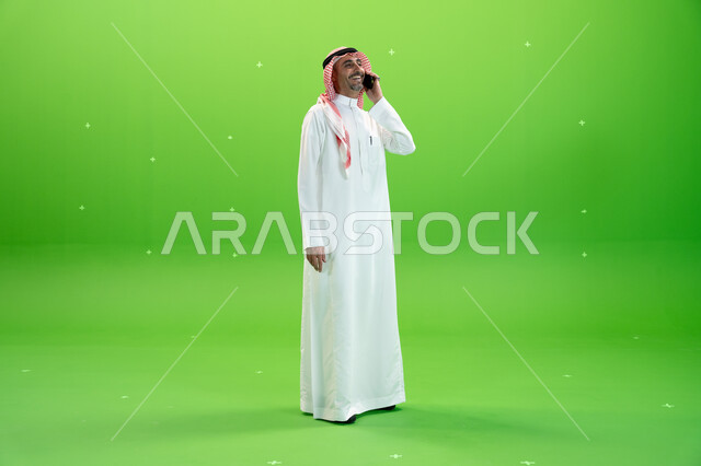 مفهوم صلة الرحم، الاتفاق على موعد عمل، كروما لرجل عربي خليجي سعودي يرتدي الثوب والشماغ السعودي يقوم بإجراء مكالمة صوتيه عبر الهاتف المحمول، التواصل مع الأصدقاء والأقارب بإيماءات السعادة، صورة الجسم بالطول الكامل، خلفية خضراء