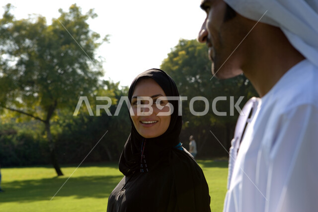 نزهة في الهواء الطلق, أجواء عائلية هادئة بإيماءات الحب والتفاهم, صورة مقربة لزوجين عربيين خليجيين إماراتيين يقومان بالمشي في إحدى الحدائق الإماراتية, الاستمتاع بقضاء وقت رومنسي هادئ, حدائق ومنتزهات الترفيه في الإمارات