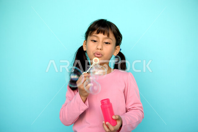 تنمية مهارات الأطفال الحركية, الاستمتاع بصنع فقاعة الصابون في الهواء, قضاء الأوقات بالأنشطة الترفيهية الممتعه والمسلية, بورتريه مقرب لفتاة عربية خليجية إماراتية تقوم بنفخ البالونات الهوائية, اللعب بالفقاعات المائية المتطايرة والمتناثرة, خلفية ملونة