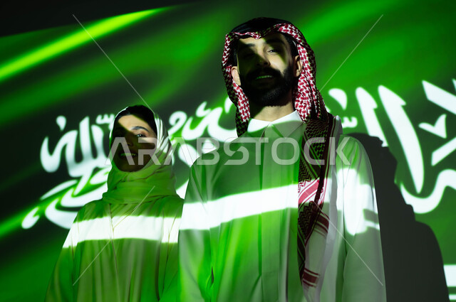 أعياد ومناسبات وطنية، إظهار التفاني والانتماء للبلاد وتعزيز الروح الوطنية، الوقوف بثقة والنظر إلى الكاميرا، صورة مقربة لانغماس جسم زوجان عربيان خليجيان سعوديان في ضوء العلم، إحياء ذكرى اليوم الوطني السعودي 23 سبتمبر، يوم العلم 11 مارس و العيد الوطني