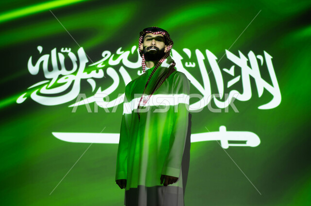 The concept of love for the homeland and belonging to it, celebrating the anniversary of the Saudi National Day, September 23, and National Day, the merging of the light of the flag with the body of a Saudi Gulf Arab man wearing traditional clothing, showing feelings of belonging and love for the country, Flag Day, March 11, traditional national celebrations and events