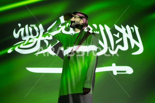 إيماءات التدقيق والمعاينة عن بعد، اندماج ضوء العلم مع الجسم، الاحتفال بيوم العلم 11مارس والعيد الوطني، احتفالات ومناسبات وطنية، رجل عربي خليجي سعودي مبتسم يرتدي الزي التقليدي يضع يديه فوق عينيه وينظر إلى شيء ما, ذكرى اليوم الوطني السعودي 23 سبتمبر