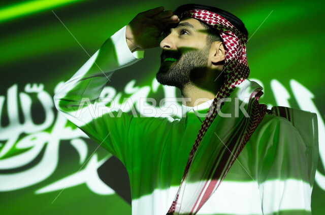الاحتفال بيوم العلم 11مارس والعيد الوطني، إيماءات المعاينة عن بعد، اندماج ضوء العلم مع الجسم، احتفالات ومناسبات وطنية، صورة مقربة لرجل عربي خليجي سعودي مبتسم يرتدي الزي التقليدي يضع يديه فوق عينيه وينظر إلى شيء ما, ذكرى اليوم الوطني السعودي 23 سبتمبر