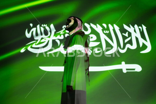 Pride in the Saudi national identity, immersion of the body in the light of the flag, a side image of a Gulf Arab man wearing traditional Saudi dress, looking at something, commemorating the Saudi National Day 93, the Saudi Flag Day on March 11, the Natio