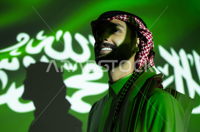 إظهار مشاعر الحب والولاء إلى السعودية، انغماس ضوء العلم مع الوجه، الاحتفال بيوم العلم 11مارس والعيد الوطني، أعياد ومناسبات وطنية ،صورة مقربة من الجانب لرجل عربي خليجي سعودي مبتسم يرتدي الزي التقليدي ينظر إلى شيء ما, ذكرى اليوم الوطني السعودي 23 سبتمبر .