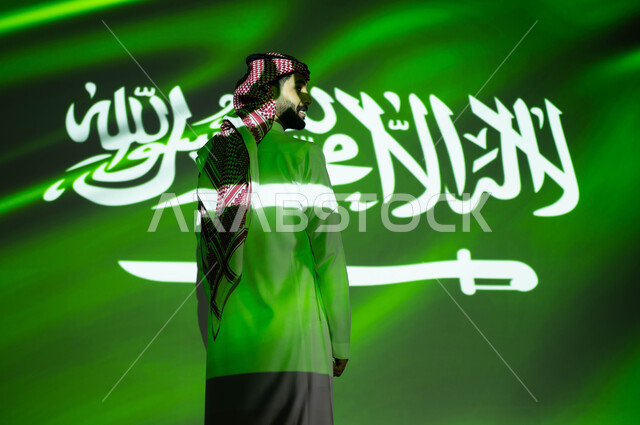 أعياد ومناسبات وطنية شعبيه، مشاعر الولاء والحب والانتماء للمملكة، انغماس الجسم في ضوء العلم، صورة من الخلف لرجل عربي خليجي سعودي يرتدي الزي التقليدي يحتفل بالعيد الوطني وينظر إلى شيء ما، إحياء ذكرى اليوم الوطني السعودي 23 سبتمبر، يوم العلم 11 مارس