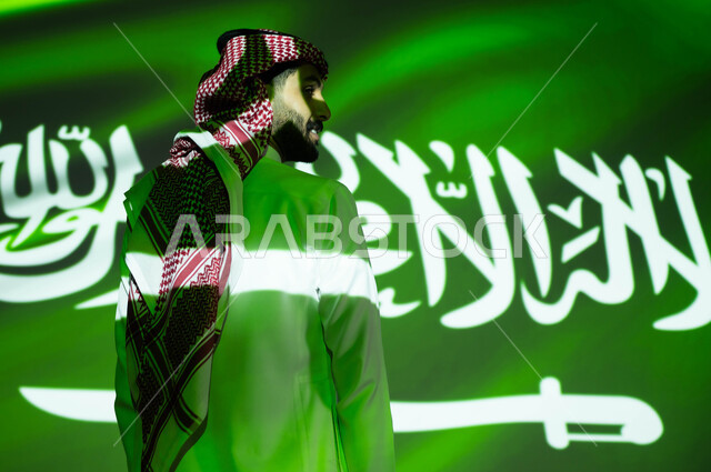 أعياد ومناسبات وطنية شعبيه، مشاعر الولاء والحب والانتماء للمملكة، انغماس الجسم في ضوء العلم، صورة من الخلف لرجل عربي خليجي سعودي يرتدي الزي التقليدي يحتفل بالعيد الوطني وينظر إلى شيء ما، إحياء ذكرى اليوم الوطني السعودي 23 سبتمبر، يوم العلم 11 مارس