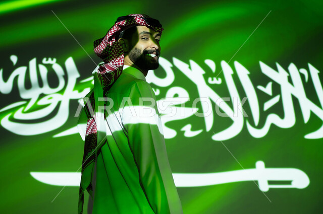 مفهوم حب الوطن والانتماء إليه، الاحتفال بذكرى اليوم الوطني السعودي 23 سبتمبر والعيد الوطني، اندماج ضوء العلم مع جسد رجل عربي خليجي يرتدي الزي التقليدي يظهر مشاعر الحب للبلاد , يوم العلم السعودي 11 مارس، احتفالات ومناسبات وطنية تقليدية