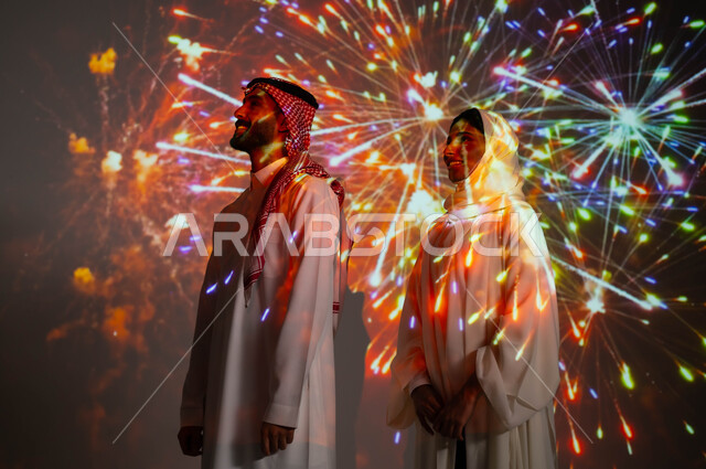 فعاليات وأنشطة ترفيهية في العيد الإسلامي المبارك، مشاركة العائلة باللحظات والذكريات السنوية، الاستمتاع بالمفرقعات والألعاب النارية في الأعياد والمناسبات الوطنية، صورة جانبية لزوجين عربيين خليجيين سعوديين مبتسمين يحتفلان بالأفراح السعيدة.
