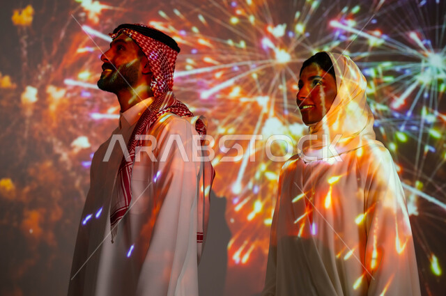 أنشطة ترفيهية وفعاليات في العيد الإسلامي المبارك، مشاركة العائلة باللحظات والذكريات السنوية، الاستمتاع بالمفرقعات والألعاب النارية في الأعياد والمناسبات الوطنية، صورة جانبية لزوجين عربيين خليجيين سعوديين مبتسمين يحتفلان بالأفراح السعيدة.
