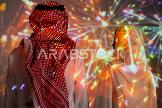 Family sharing moments and anniversaries, enjoying firecrackers and fireworks on holidays and national occasions, a picture from behind of a Saudi Arabian Gulf couple celebrating happy joys, entertainment activities and events on the blessed Islamic Eid.