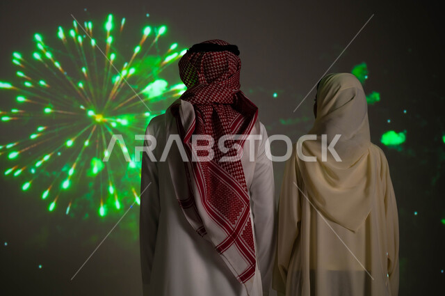 الحفاظ على الهوية الوطنية و الاعتزاز والفخر بتراثها، التعبير عن الحب والولاء للبلاد ،الاستمتاع بالألعاب النارية في المناسبات والأعياد الشعبيه، صورة من الخلف لزوجين عربيين خليجيين سعوديين يحتفلان بذكرى اليوم الوطني السعودي في23 سبتمبر والعيد الوطني