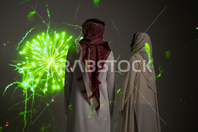 الحفاظ على الهوية السعودية و الاعتزاز والفخر بتراثها، التعبير عن الحب والولاء للبلاد ،الاستمتاع بالألعاب النارية في المناسبات والأعياد الوطنية، صورة من الخلف لزوجين عربيين خليجيين سعوديين يحتفلان بذكرى اليوم الوطني السعودي في23 سبتمبر والعيد الوطني