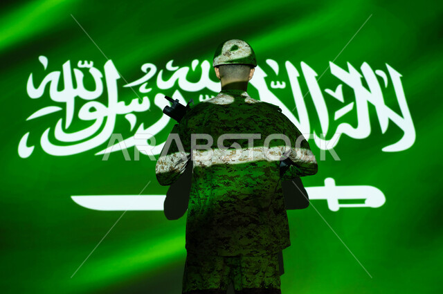 انعكاس ضوء العلم على الجسم، إحياء ذكرى اليوم الوطني السعودي 23 سبتمبر، الاحتفال بالعيد الوطني ، يوم العلم 11 مارس، صورة من الخلف لجندي عربي خليجي سعودي يرتدي الزي العسكري والخوذة يحمل السلاح، حماية الجنود الوطن والدفاع عنه، الاخلاص والولاء للبلاد