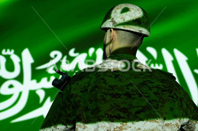 انعكاس ضوء العلم على الجسم، إحياء ذكرى اليوم الوطني السعودي 23 سبتمبر، الاحتفال بالعيد الوطني ، يوم العلم 11 مارس، صورة مقربة من الخلف لجندي عربي خليجي سعودي يرتدي الزي العسكري والخوذة يحمل السلاح، حماية الجنود الوطن والدفاع عنه.