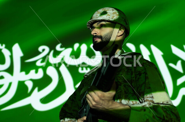 تعزيز القوات العسكرية لزيادة الأمن والاستقرار في السعودية، إحياء ذكرى اليوم الوطني السعودي 23 سبتمبر، انغماس الجسم في ضوء العلم، الاحتفال بالعيد الوطني، يوم العلم 11 مارس، صورة مقربة لجندي عربي خليجي يرتدي الزي العسكري والخوذة يحمل السلاح.