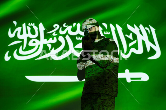 الاحتفال بذكرى اليوم الوطني 23 سبتمبر و العيد الوطني، انعكاس ضوء العلم على جسم الشاب، يوم العلم 11 مارس، جندي عربي خليجي يرتدي الزي العسكري والخوذة يحمل السلاح، تعزيز القوات العسكرية لزيادة الأمن والحماية والاستقرار في المملكة العربية السعودية.