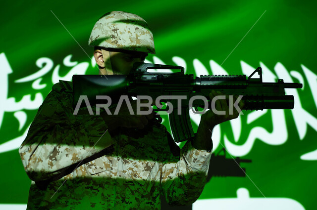 انعكاس ضوء علم المملكة على جسد الشاب، حماية الوطن والدفاع عنه، الاحتفال بذكرى اليوم الوطني السعودي 23 سبتمبر و العيد الوطني، يوم العلم 11 مارس، صورة مقربة لجندي عربي خليجي سعودي يرتدي الزي العسكري والخوذة و يحمل السلاح، حفظ الأمن والاستقرار بقوات الجيش السعودي