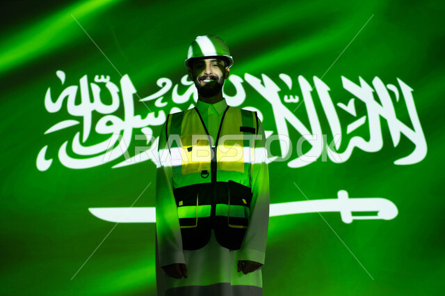 Engineering development and growth in the construction sector with the hands of the people of the country, looking at the camera, a smiling Saudi Arabian Gulf engineer wearing a jacket and a protective helmet, immersing the body in the light of science, Science Day, March 11, celebrating the anniversary of the Saudi National Day, September 23, and National Day, Saudi professions and jobs
