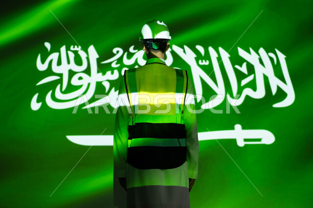 التطور والنمو العمراني للمباني والمنشآت بسواعد أبناء الوطن, الاخلاص والحب للبلاد ،صورة من الخلف لمهندس عربي خليجي سعودي يرتدي السترة وخوذة الحماية، انغماس الجسم بضوء العلم، يوم العلم 11 مارس، الإحتفال بذكرى اليوم الوطني السعودي 23 سبتمبر والعيد الوطني