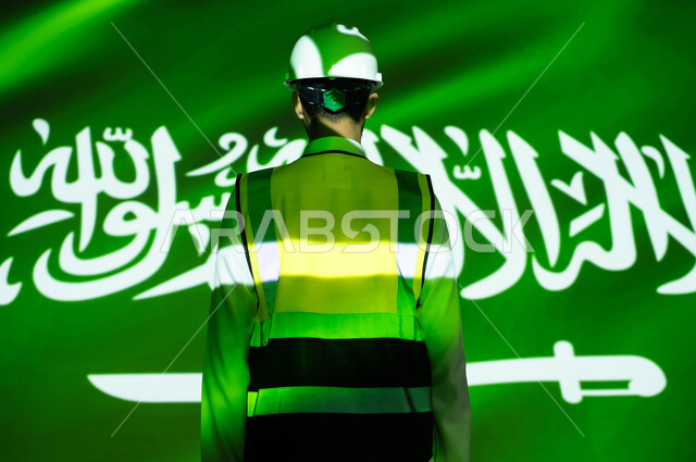التطور والنمو العمراني للمباني والمنشآت بسواعد أبناء الوطن, الاخلاص والحب للبلاد ،صورة من الخلف لمهندس عربي خليجي سعودي يرتدي السترة وخوذة الحماية، انغماس الجسم بضوء العلم، يوم العلم 11 مارس، الإحتفال بذكرى اليوم الوطني السعودي 23 سبتمبر والعيد الوطني