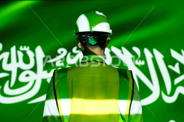 التطور والنمو العمراني للمباني والمنشآت بسواعد أبناء الوطن, صورة من الخلف لمهندس عربي خليجي سعودي يرتدي السترة وخوذة الحماية، انغماس الجسم بضوء العلم، يوم العلم 11 مارس، الإحتفال بذكرى اليوم الوطني السعودي 23 سبتمبر والعيد الوطني