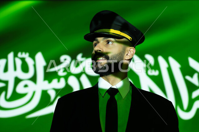 مهنة الملاحة الجوية والطيران في السعودية، احياء ذكرى اليوم الوطني السعودي في 23 سبتمبر، الاحتفال بيوم العلم 11 مارس والعيد الوطني، صورة مقربة لانعكاس ضوء العلم على وجه كابتن طائرة عربي خليجي سعودي مبتسم، خلفية العلم السعودي الأخضر المضيء