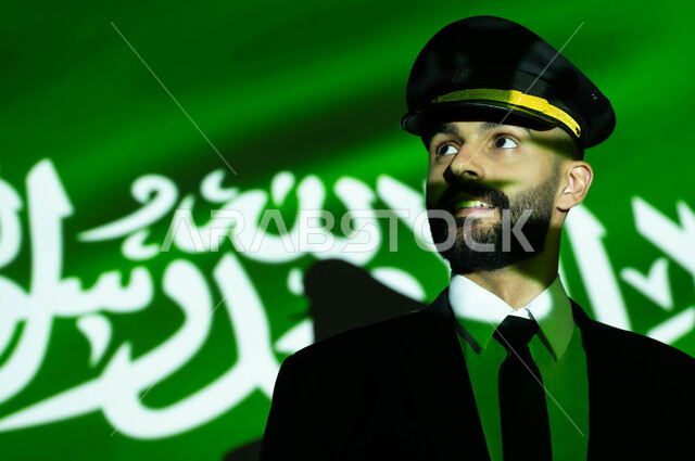 The profession of aeronautics and aviation in Saudi Arabia, commemorating the Saudi National Day on September 23, celebrating Flag Day on March 11 and National Day, a close-up image of the reflection of the light of the flag on the face of a smiling Saudi Gulf Arab plane captain, the background of the luminous green Saudi flag