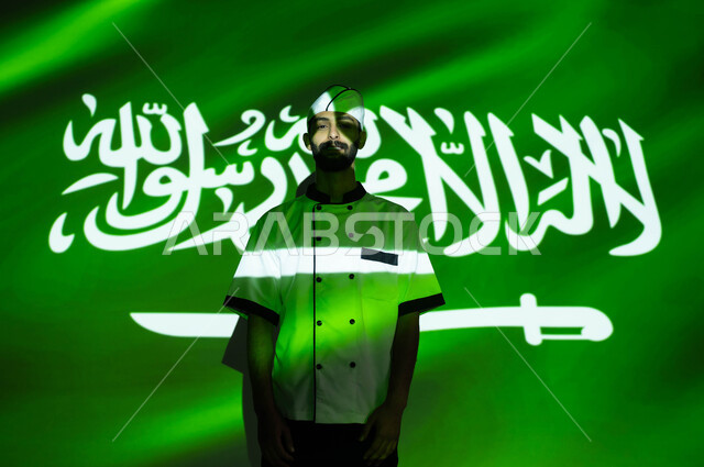 نهضة البلاد بالمهن السعوديه المختلفه، نظرات الفخر والااعتزاز بالبلاد، الإحتفال في العيد الوطني و يوم العلم 11 مارس، اليوم الوطني السعودي 8 ربيع الأول، صورة مقربة لطباخ عربي خليجي سعودي مبتسم يرتدي زي الشيف ، اندماج الوجه بضوء العلم، الحب والاخلاص للوطن