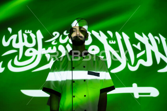 نهضة وتطور البلاد بالمهن السعوديه المختلفه، نظرات الفخر والااعتزاز بالبلاد، الإحتفال في العيد الوطني و يوم العلم 11 مارس، اليوم الوطني السعودي 8 ربيع الأول، صورة مقربة لطباخ عربي خليجي سعودي مبتسم يرتدي زي الشيف ، اندماج الوجه بضوء العلم، الحب والاخلاص للوطن