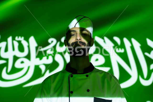 نهضة وتطور البلاد بالمهن السعوديه المختلفه، نظرات الفخر والااعتزاز بالبلاد، الإحتفال في العيد الوطني و يوم العلم 11 مارس، اليوم الوطني السعودي 8 ربيع الأول، صورة مقربة لطباخ عربي خليجي سعودي مبتسم يرتدي زي الشيف ، اندماج الوجه بضوء العلم، الحب والاخلاص للوطن