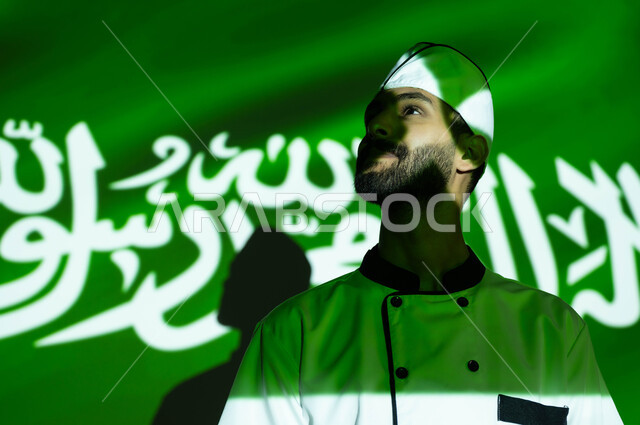 تطور ونهضة البلاد بالمهن السعوديه المختلفه، نظرات الفخر والاعتزاز بالبلاد، اليوم الوطني السعودي 8 ربيع الأول، الإحتفال في العيد الوطني و يوم العلم 11 مارس، صورة مقربة لطباخ عربي خليجي سعودي مبتسم يرتدي زي الشيف ، اندماج الوجه بضوء العلم، الحب والاخلاص للوطن
