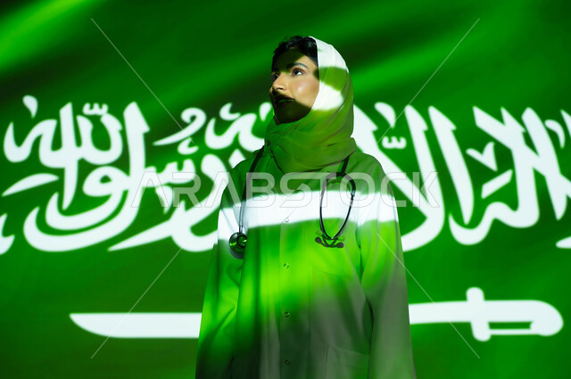 تقديم الخدمات العلاجية والرعاية الصحية لأبناء الوطن، انعكاس ضوء العلم على وجه طبيبة عربية خليجية سعودية محجبة ترتدي المعطف الطبي ، اليوم الوطني السعودي 23 سبتمبر، الاحتفال بيوم العلم السعودي 11 مارس والعيد الوطني، مهن ووظائف نسائية