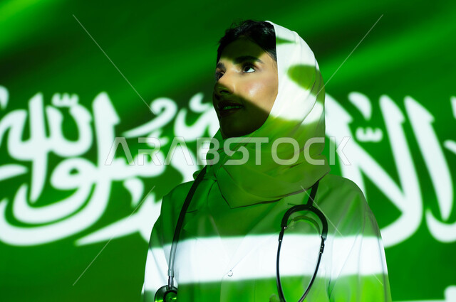 انعكاس ضوء العلم على الوجه، تقديم الرعاية الصحية لأبناء الوطن، صور مقربة لطبيبة عربية خليجية سعودية محجبة ترتدي المعطف الطبي ، اليوم الوطني السعودي 23 سبتمبر، الاحتفال بيوم العلم السعودي 11 مارس والعيد الوطني، مهن ووظائف نسائية