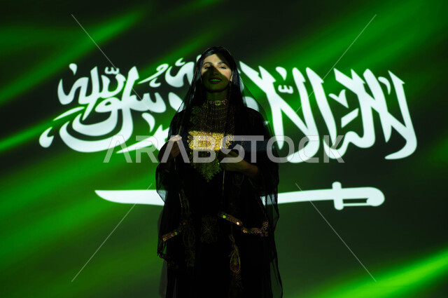 Commemoration of the Founding Day 1727 AD, national popular holidays and events, celebration of Flag Day on March 11, commemoration of the Saudi National Day on September 23, a smiling Saudi Gulf Arab woman wearing the sheila and the dress of the central region on National Day, immersion of the body in the light of science, loyalty and love for the Kingdom