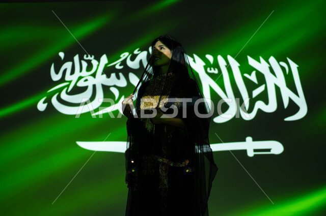 الاعتزاز والفخر بإنجازات الوطن وثقافته، يوم العلم 11 مارس، الاحتفال بذكرى اليوم الوطني السعودي 23 سبتمبر، شابه عربية خليجية سعودية مبتسمة ترتدي الشيلة وثوب المنطقة الوسطى في العيد الوطني، احتفالات ومناسبات وطنية، انعكاس ضوء العلم على الوجه، يوم التأسيس 1727 م