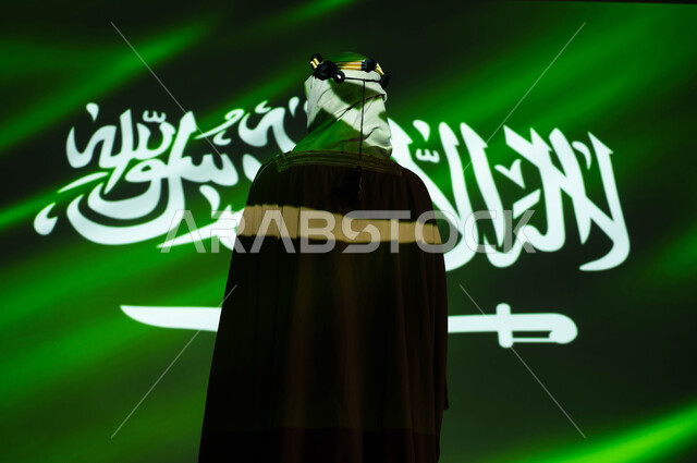 انغماس الجسم في ضوء العلم، إحياء ذكرى اليوم الوطني السعودي 8 ربيع الاول، تأسيس الدولة السعودية 1727 م ،اظهار التفاني للبلاد، يوم العلم 11 مارس، صورة من الخلف لرجل عربي خليجي سعودي يرتدي البشت والغترة في العيد الوطني، الزي الشعبي التقليدي للمنطقة الجنوبية