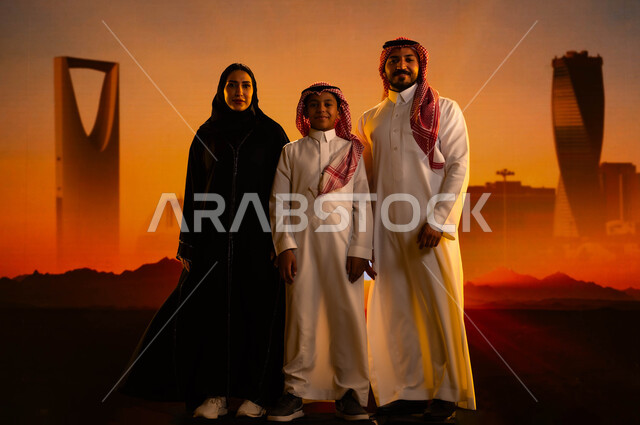 رؤية السعودية المستقبلية 2030، عائلة عربية خليجية سعودية تقف بثقة وتنظر إلى الكاميرا، النمو والتطور العمراني في السعودية، الإنشاءات والهندسة المعمارية، مفهوم الترابط الأسري، صورة الجسم بالطول الكامل، خلفية الأبراج وناطحات السحاب في الرياض وقت غروب الشمس