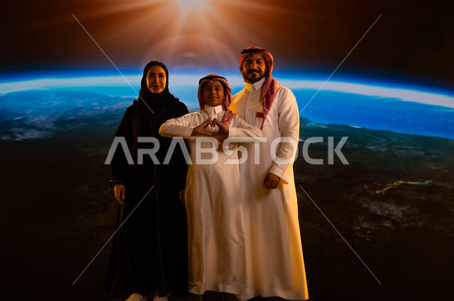 مفهوم الترابط الأسري وحب الأبناء، عائلة عربية خليجية سعودية تقف بثقة وتنظر إلى الكاميرا، إيماءات السرور والسعادة، طفل يقوم بحركة يد تدل على الحب، رحلة السعودية إلى الفضاء الخارجي، نمو وتطور قطاع الفضاء في المملكة، خلفية شروق الشمس على كوكب الأرض