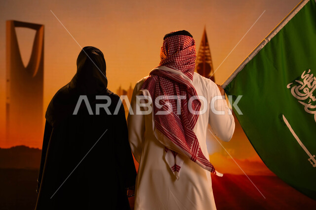 النمو والتطور العمراني، صورة من الخلف لرجل عربي خليجي سعودي يقف بجانب زوجته ويحمل علم المملكة، يوم العلم 11 مارس، العيد الوطني السعودي، اليوم الوطني لتوحيد السعودية 23 سبتمبر، رؤية السعودية المستقبلية 2030، أبراج وناطحات سحاب الرياض وقت غروب الشمس