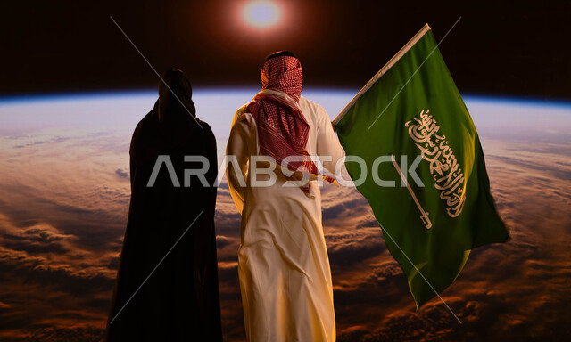 شروق الشمس على الكرة الأرضية، صورة من الخلف لرجل عربي خليجي سعودي يقف بجانب زوجته ويحمل علم السعودية، التفاني والإنتماء للوطن، اليوم الوطني لتوحيد المملكة 8 ربيع الأول، الإحتفال بالعيد الوطني السعودي، يوم العلم السعودي 11 مارس