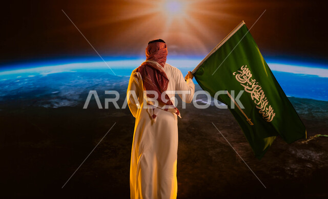 العيد الوطني السعودي 8 ربيع الاول، صورة من الخلف لرجل عربي خليجي سعودي يرتدي الشماغ والثوب الأبيض ويحمل علم المملكة ويقف امام كوكب الأرض، مفهوم  حب الوطن، ذكرى اليوم الوطني السعودي، يوم العلم 11 مارس، رحلة السعودية إلى الفضاء الخارجي
