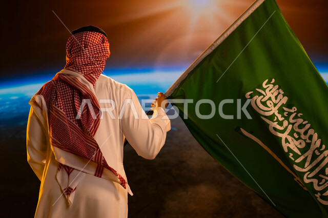 ذكرى اليوم الوطني السعودي، صورة من الخلف لرجل عربي خليجي سعودي يرتدي الشماغ والثوب الأبيض ويحمل علم السعودية وينظر الى الكرة الأرضية، العيد الوطني 8 ربيع الأول، يوم العلم السعودي 11 مارس، إيماءات الفخر والاعتزاز بالوطن، شروق الشمس على الأرض