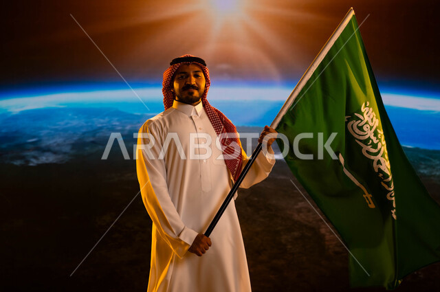 يوم العلم السعودي 11 مارس، رجل عربي خليجي سعودي يرتدي الثوب الابيض والشماغ ينظر إلى الكاميرا ويحمل علم المملكة بإيماءات الفخر والإعتزاز بالوطن، الإحتفال باليوم الوطني لتوحيد السعودية، ذكرى العيد الوطني 23 سبتمبر، نمو وتطور قطاع الفضاء، خلفية الكرة الأرضية