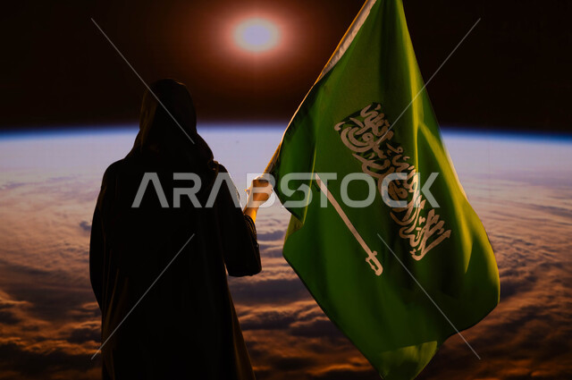 الإحتفال بذكرى اليوم الوطني السعودي، العيد الوطني 8 ربيع الاول، رحلة السعودية للفضاء الخارجي، صورة من الخلف لامرأة سعودية عربي خليجية محجبة تحمل العلم السعودي بفخر وإعتزاز، كوكب الارض وقت شروق الشمس، إستذكار التاريخ والهوية الوطنية، يوم العلم 11 مارس