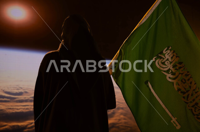 العيد الوطني 8 ربيع الاول، رحلة السعودية للفضاء الخارجي، صورة من الخلف لامرأة سعودية عربي خليجية محجبة تحمل العلم السعودي بفخر وإعتزاز، كوكب الارض وقت شروق الشمس، إستذكار التاريخ والهوية الوطنية، يوم العلم 11 مارس، الإحتفال بذكرى اليوم الوطني السعودي